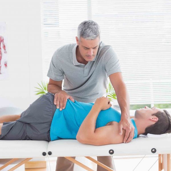 Doctor stretching a young man back in medical office